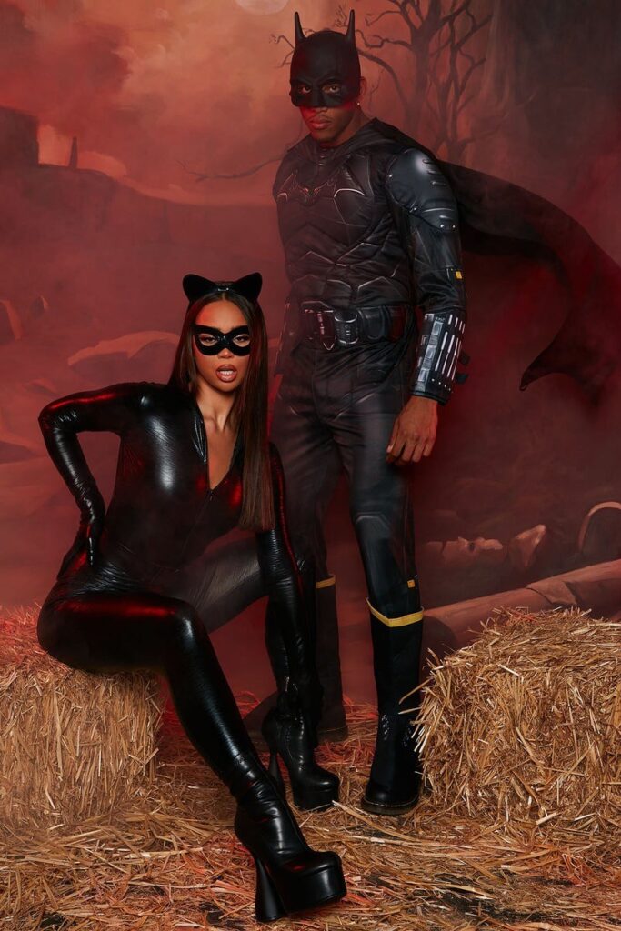 A man dressed in a Batman suit standing behind a woman posing in a black leather Catwoman jumpsuit with cat ears and an eye mask.